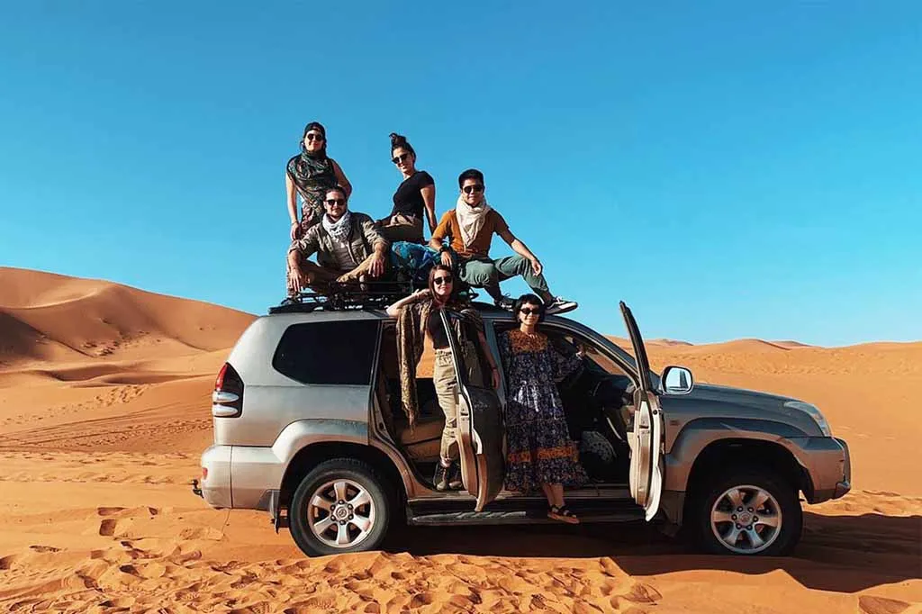 Travelers posing on a 4x4 vehicle in the Sahara dunes