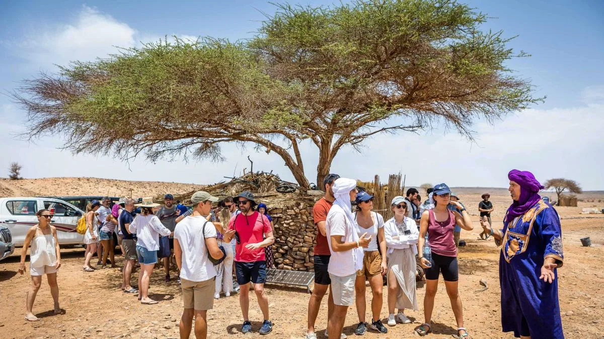 Students listening to a nomad guide under an acacia tree in the desert