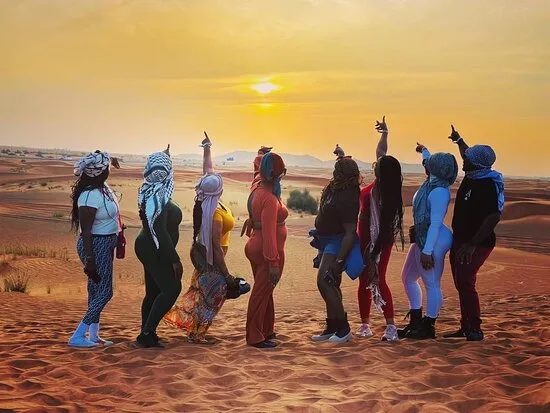 Student group in headscarves pointing at the sunset over the Sahara dunes